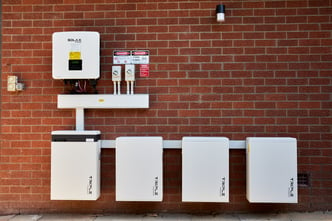 Photo of a brick wall with a Reposit installation of a solar inverter and four batteries